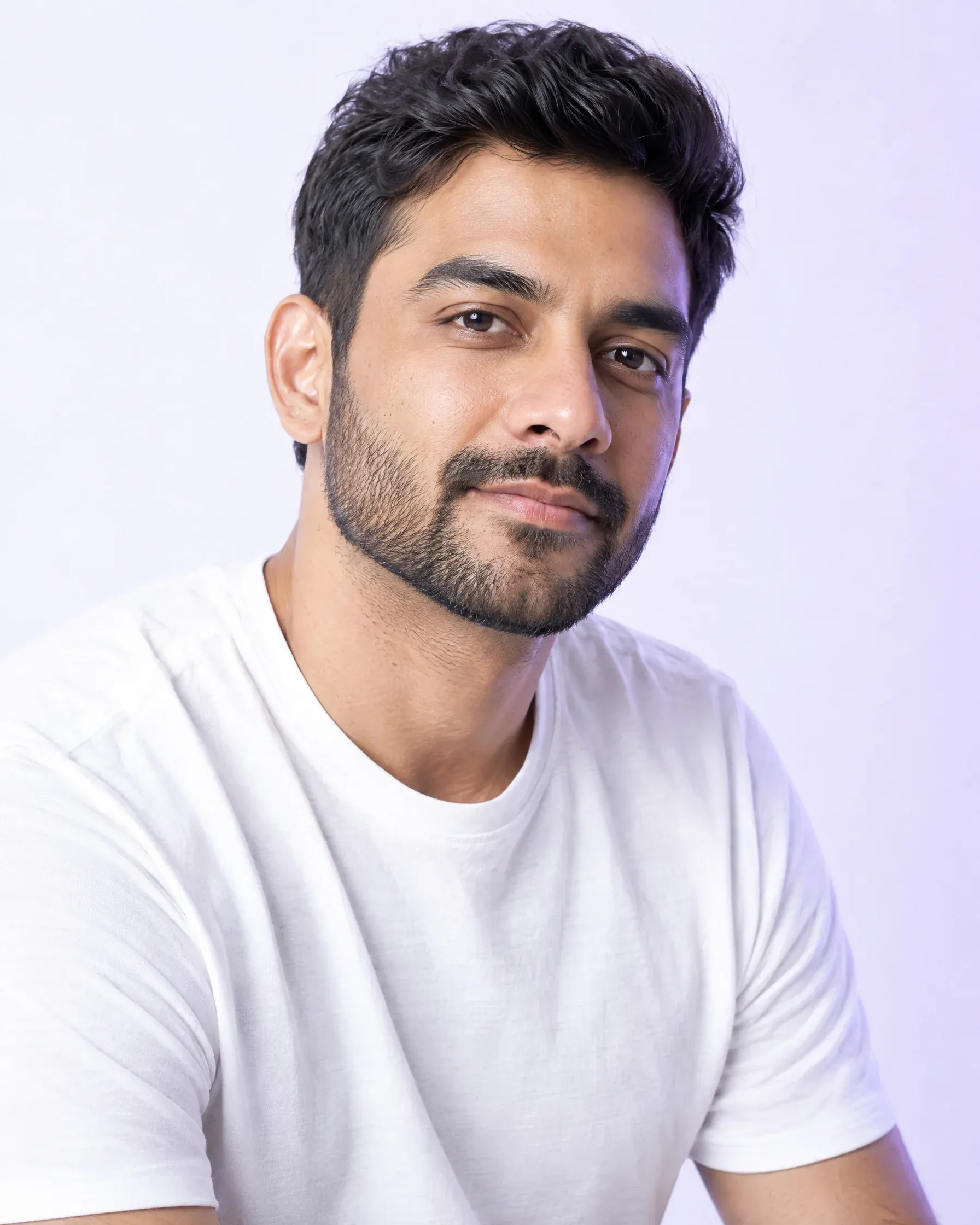 AI-generated editorial portrait of a man with a short beard in a white t-shirt, in a bright studio. A model image, not a patient or a member of staff.